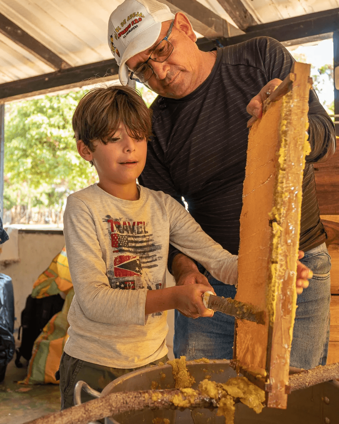 Un niño sostiene un marco de panal junto a un adulto.