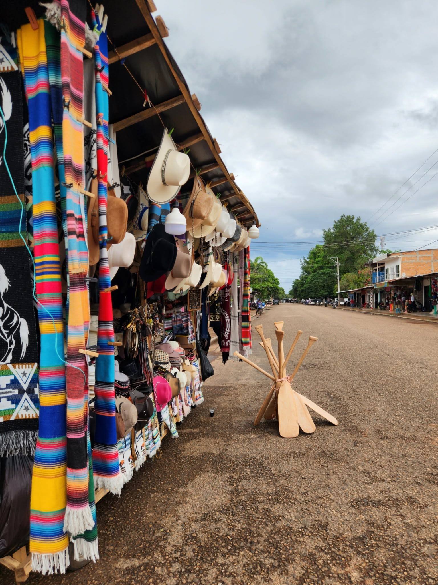 Un puesto en la calle con cobijas de colores, sombreros y canaletes de madera.