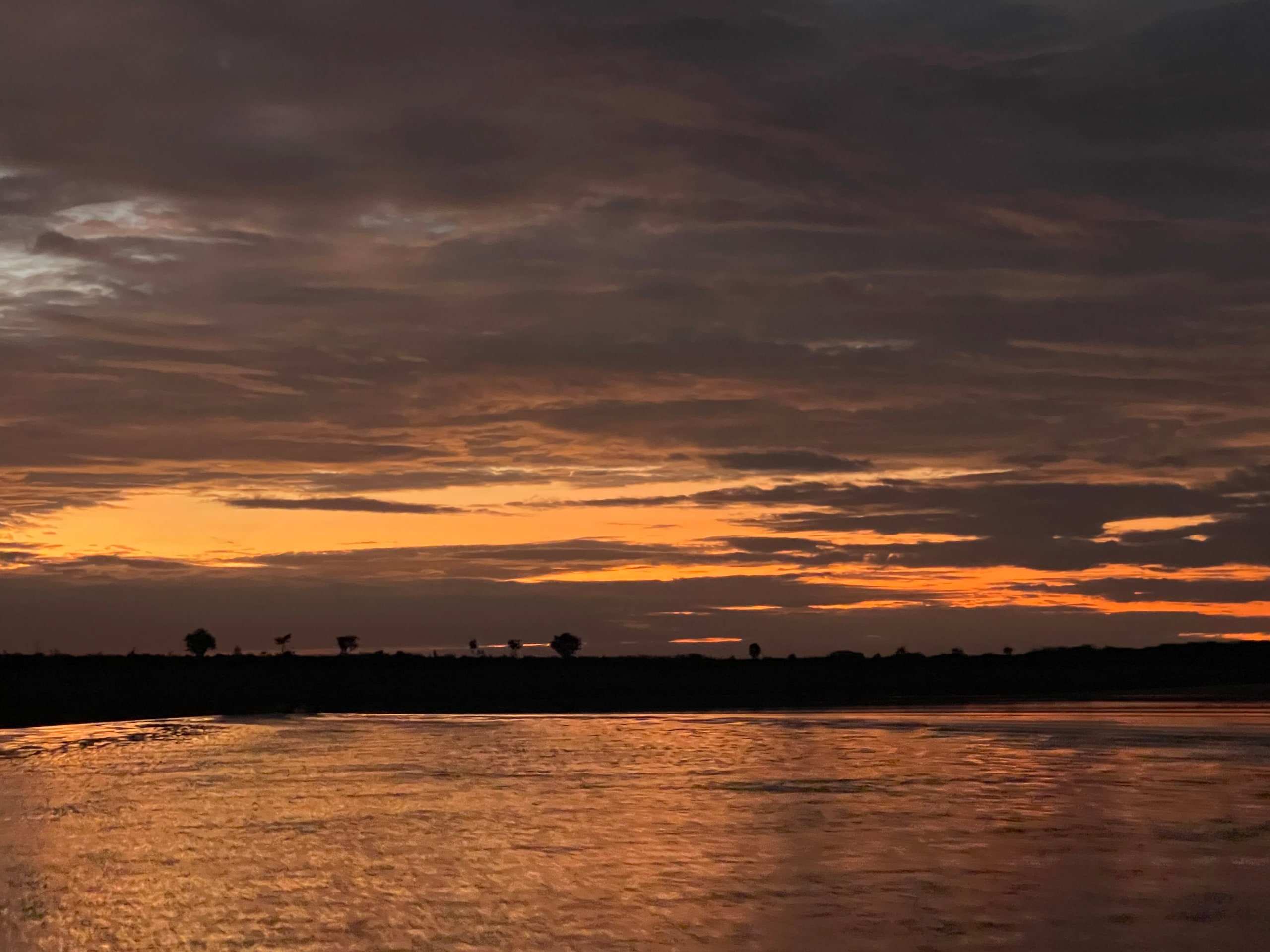 Atardecer naranja reflejado en el río, con la línea del monte al fondo.