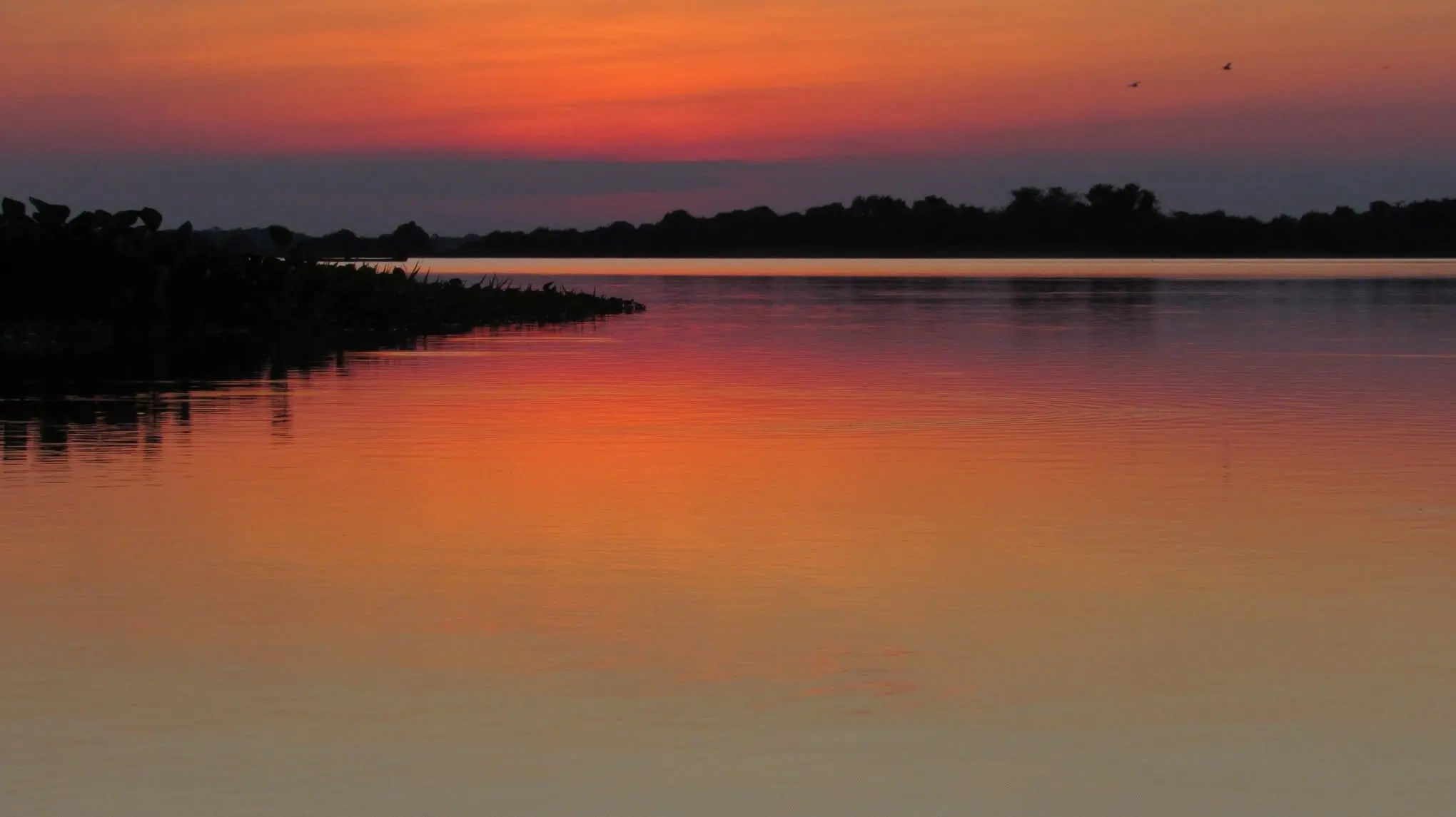 El agua de la laguna refleja el rojo del cielo cuando cae la tarde.