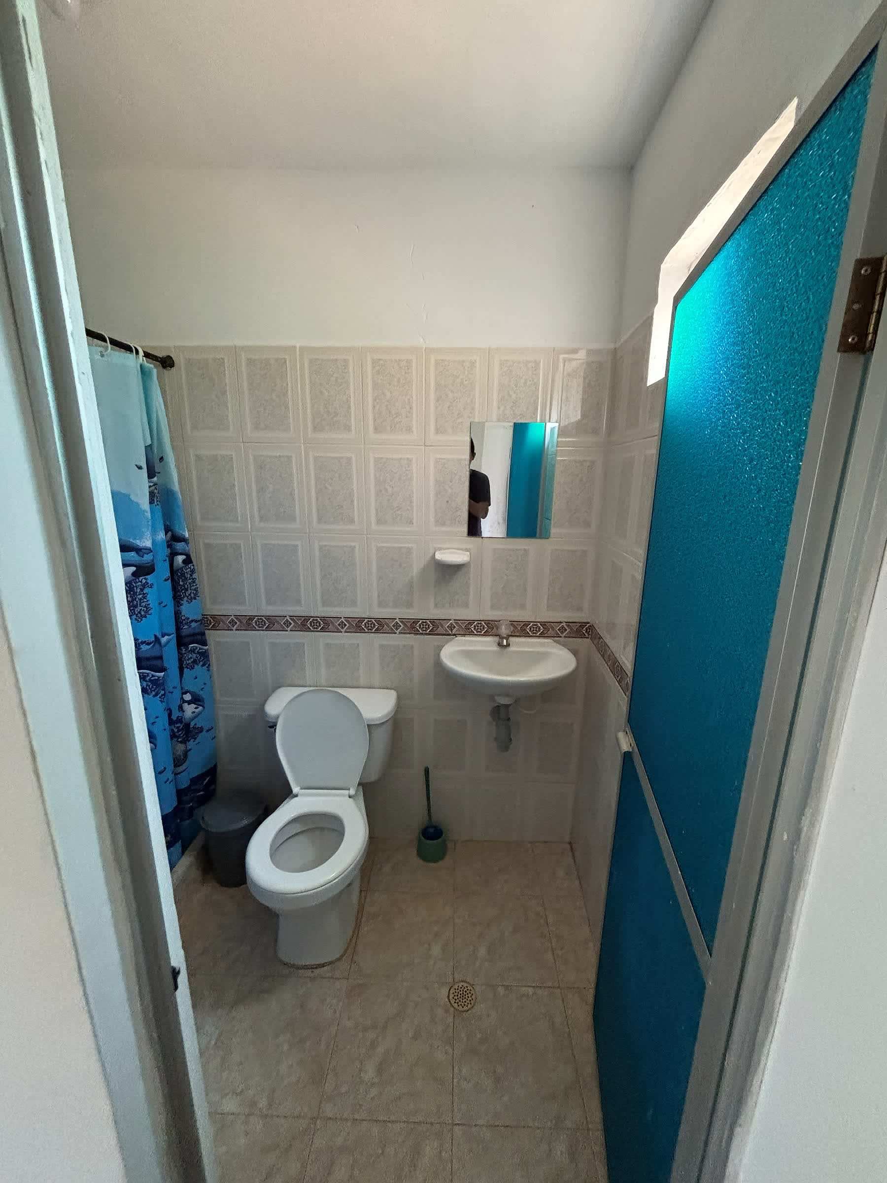 Baño privado con sanitario, lavamanos, paredes de baldosa blanca y cortina de ducha azul.