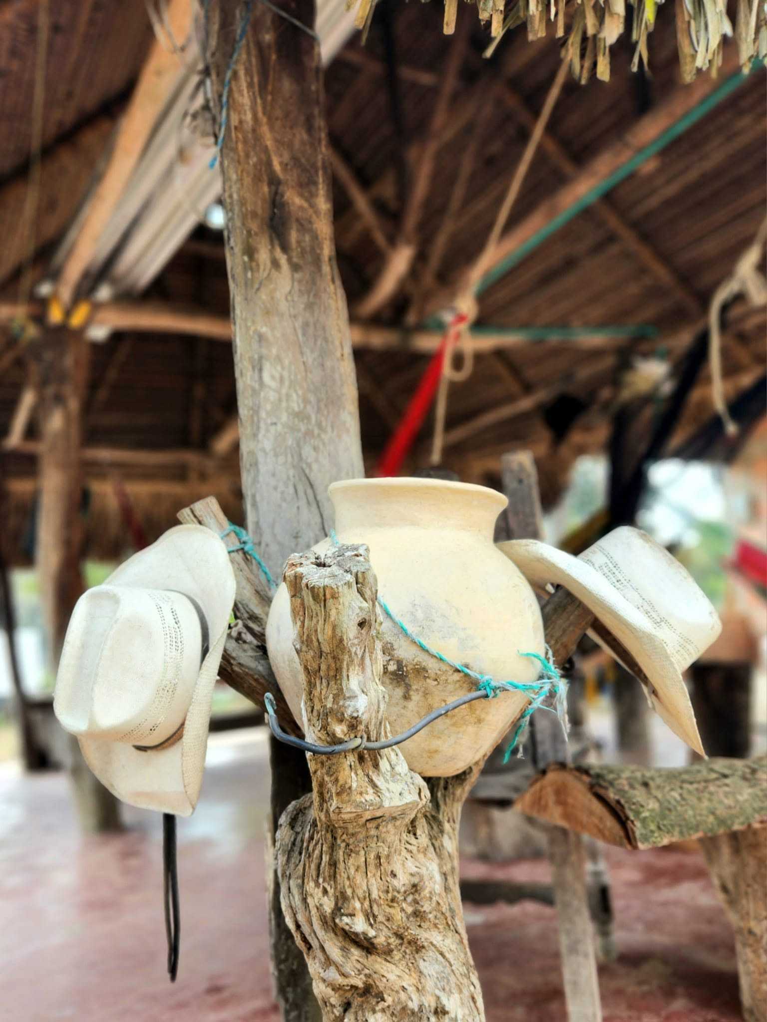 Dos sombreros llaneros y una tinaja de barro amarrados a un horcón, bajo el techo de palma de un caney.