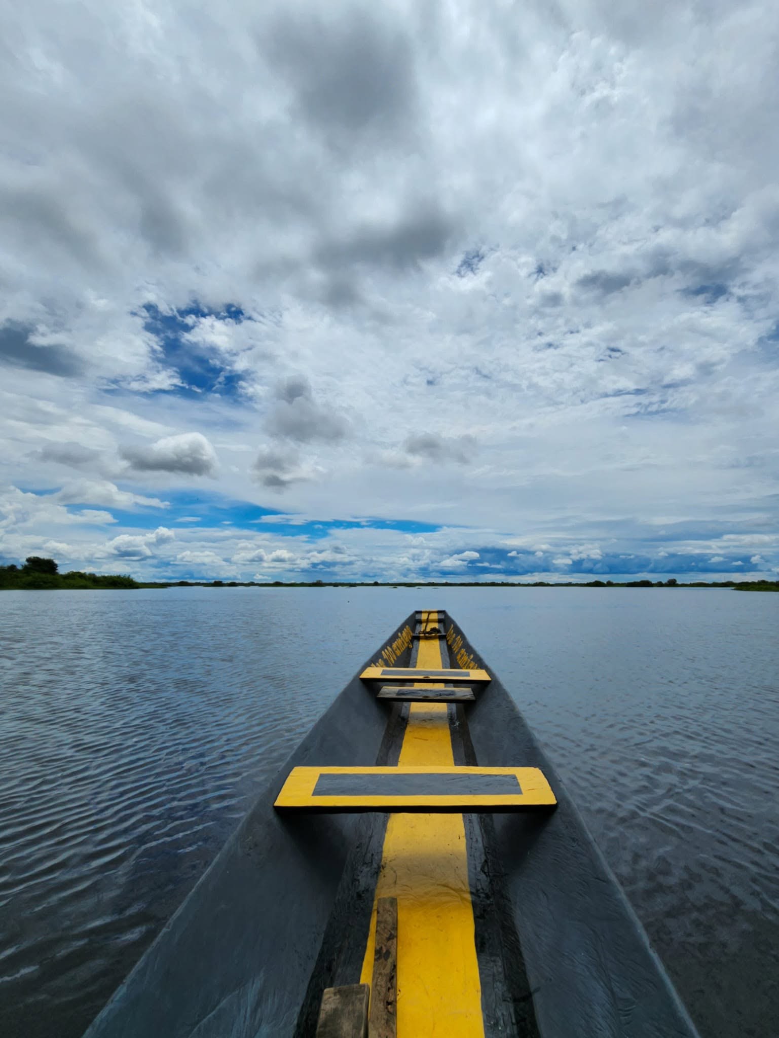 Proa de una canoa sobre la laguna, con nubes en el cielo.