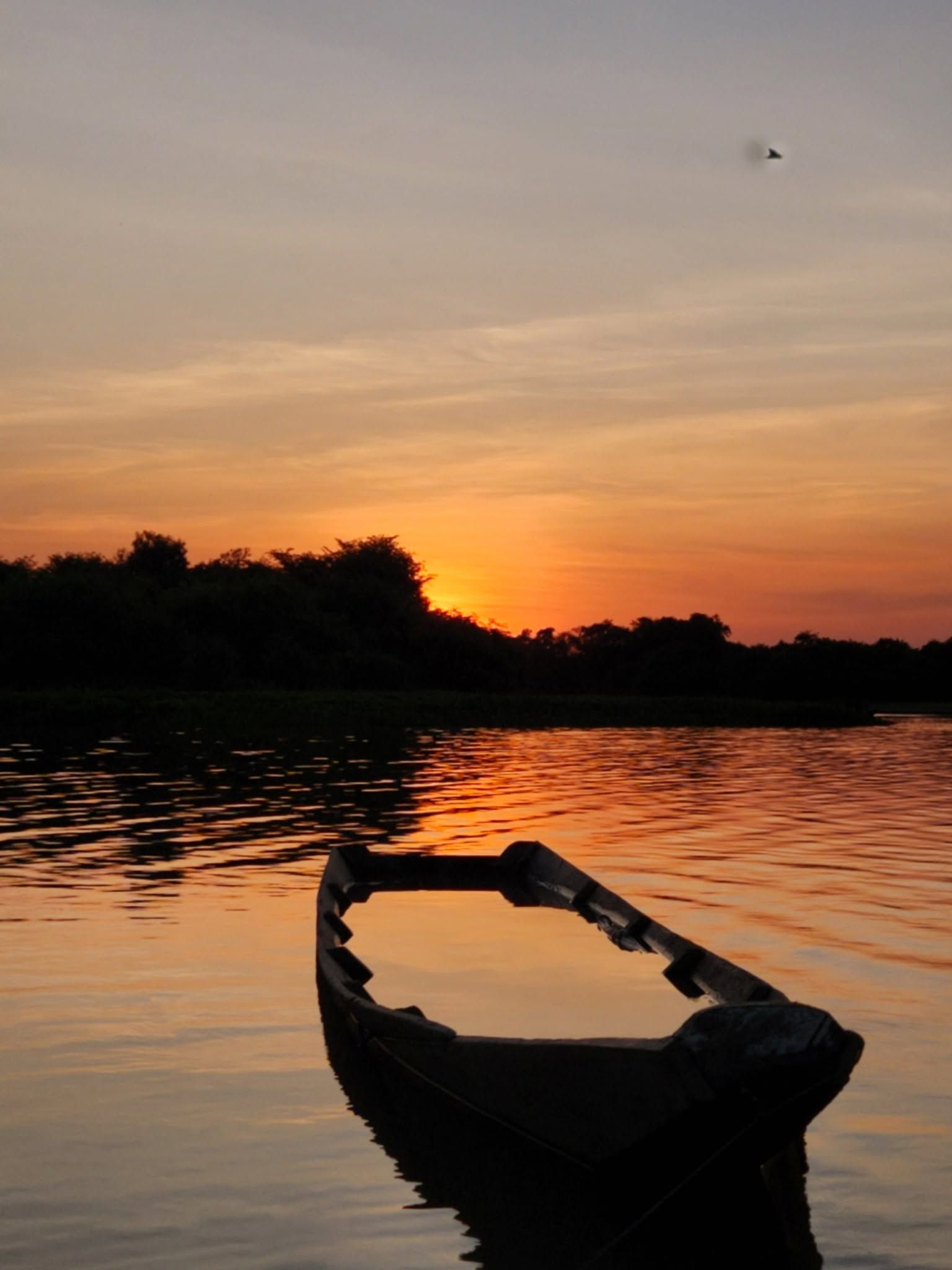 Una canoa en silueta sobre el agua quieta, con el sol cayendo detrás del monte.