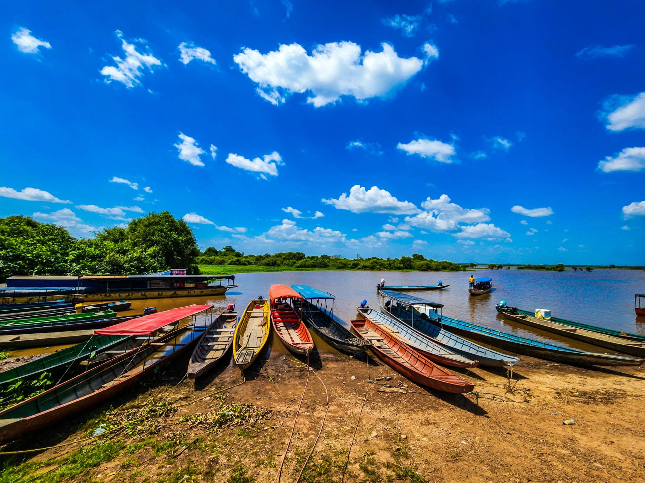 Canoas de colores en la orilla de la laguna, bajo un cielo azul con nubes.