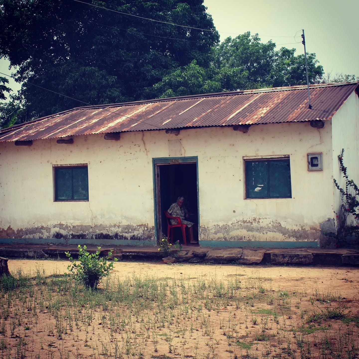 Casa antigua de bahareque con techo de zinc y un patio de tierra.