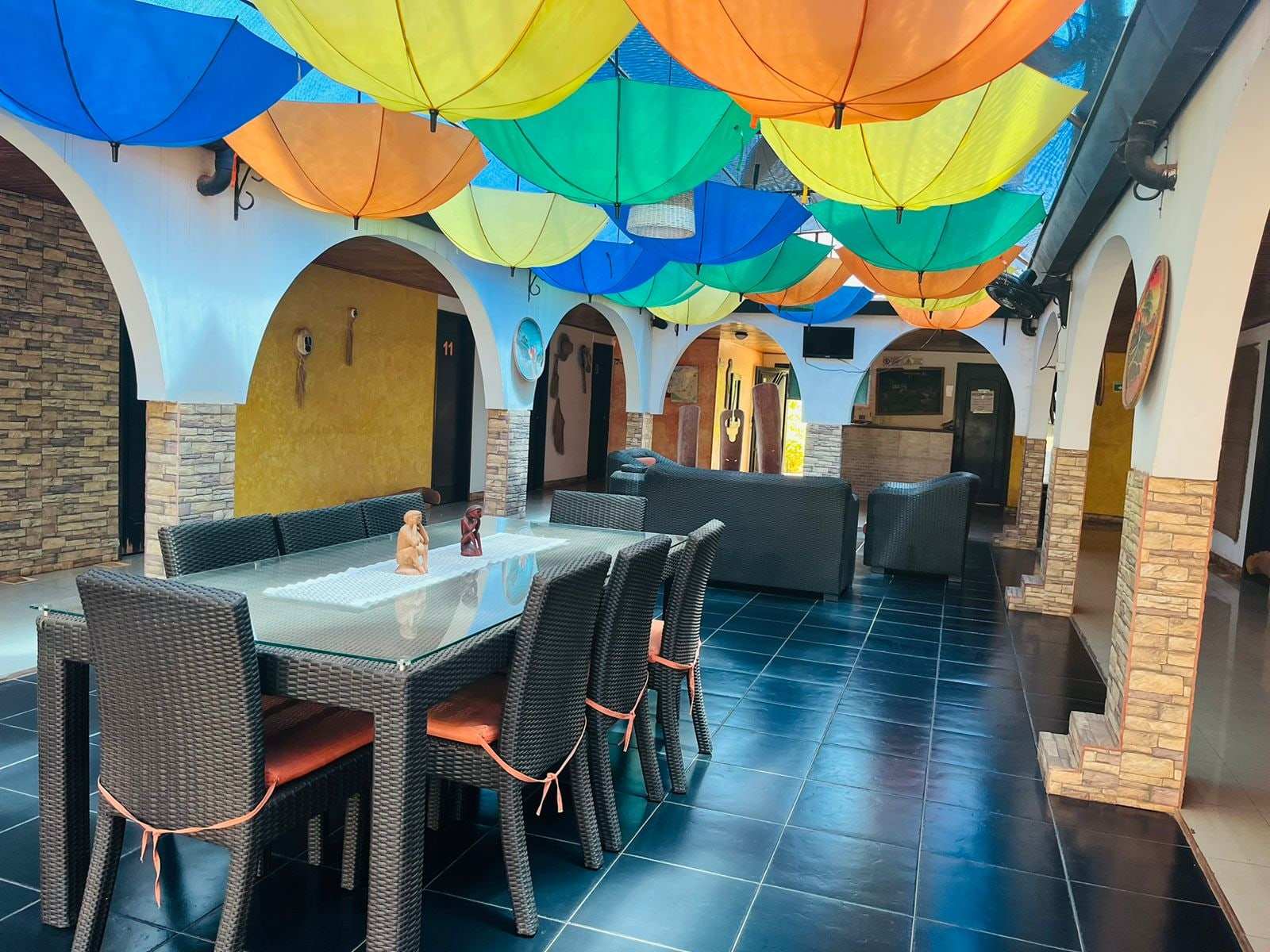 Comedor bajo sombrillas de colores, con una mesa larga y sillas oscuras entre arcos.