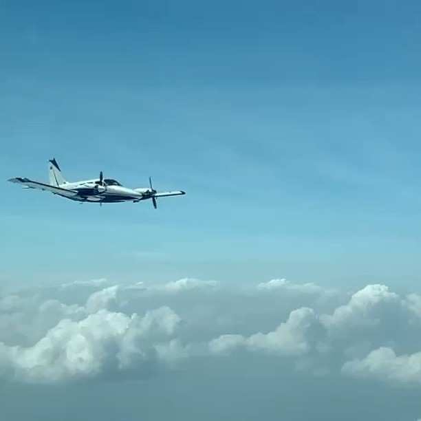 Avioneta bimotor en vuelo sobre un mar de nubes, con el cielo azul.