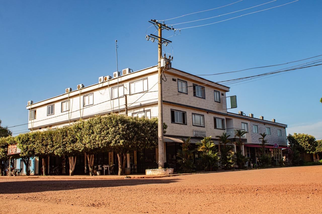 Fachada del Hotel Sol del Llano, edificio de tres pisos con árboles al frente y calle de tierra roja.