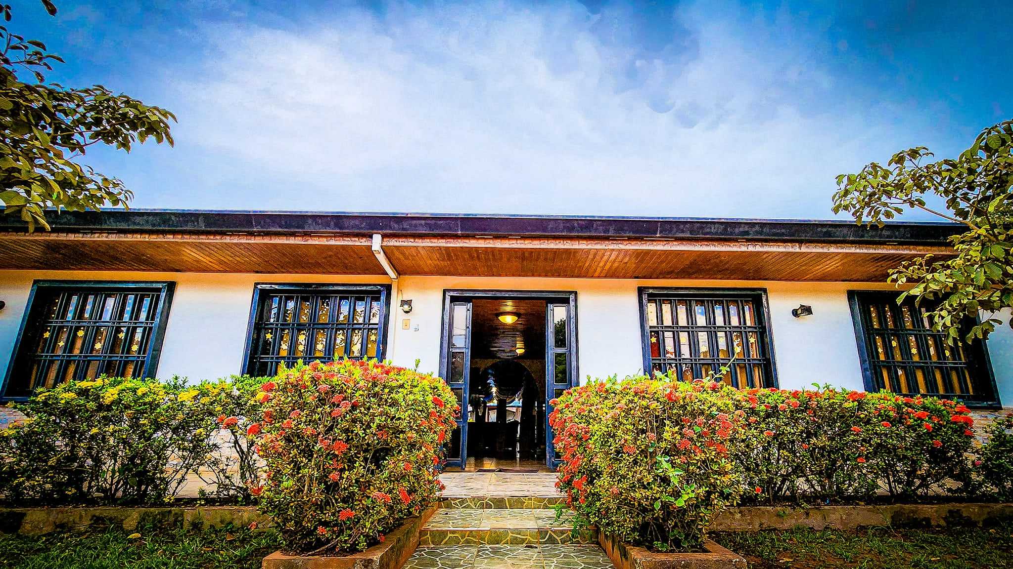 Fachada blanca del Hotel California con ventanas de reja negra y matas de flores rojas a la entrada.