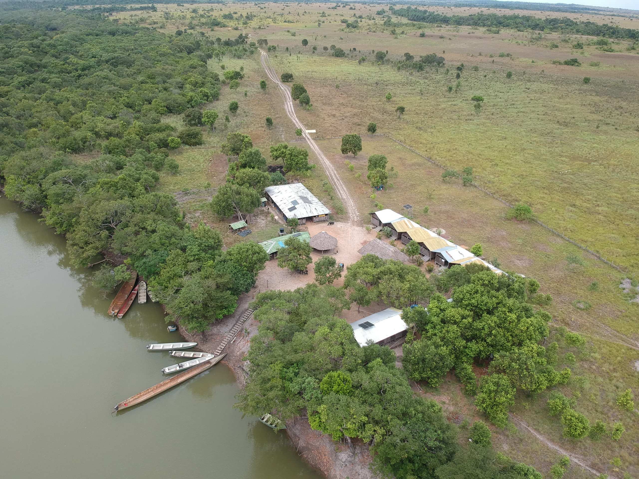 Vista aérea del Eco Hotel El Tomo: cabañas entre árboles a la orilla del río y lanchas en la playa.