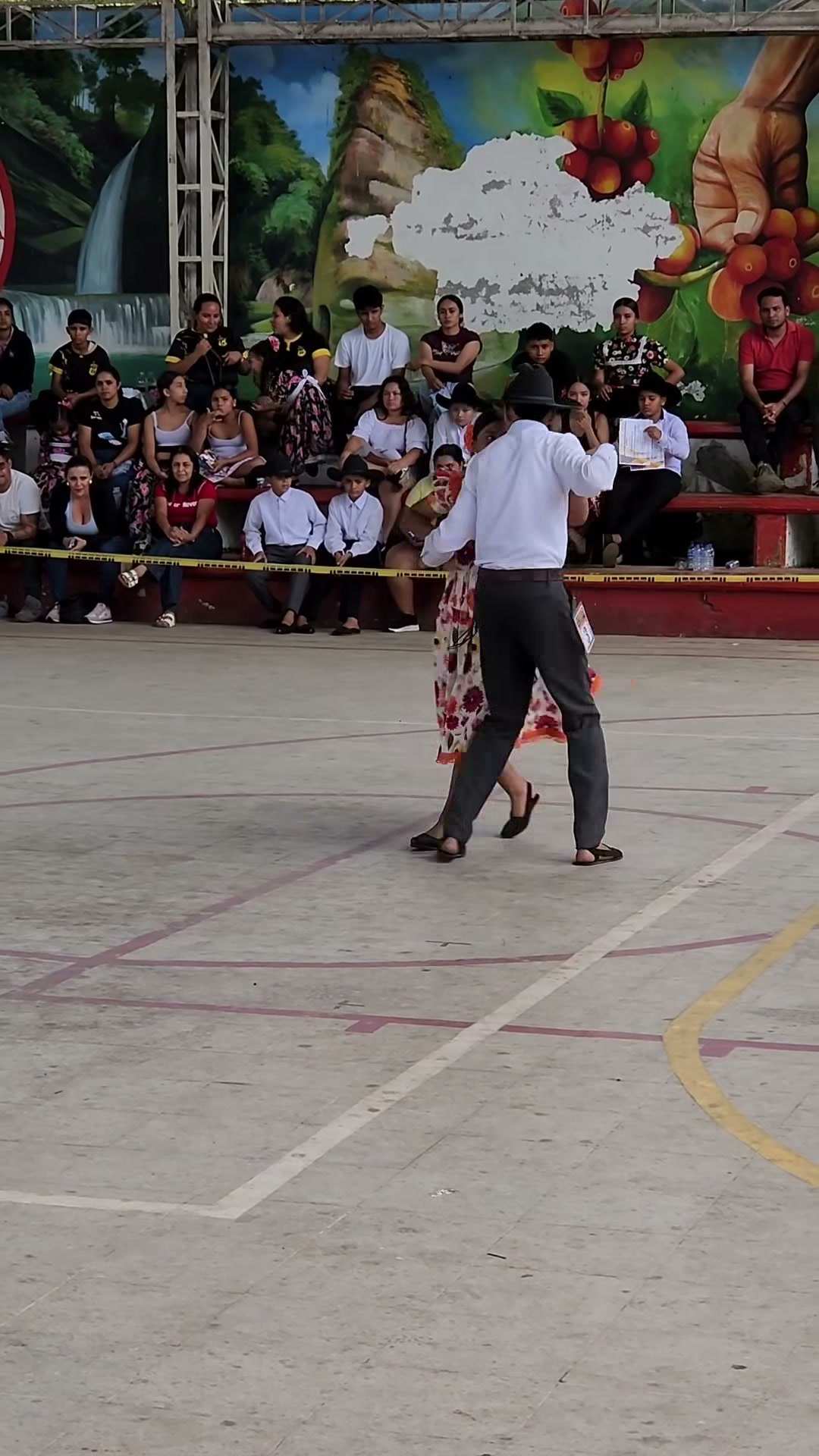 Una pareja baila joropo en la cancha cubierta, con el público en las gradas.