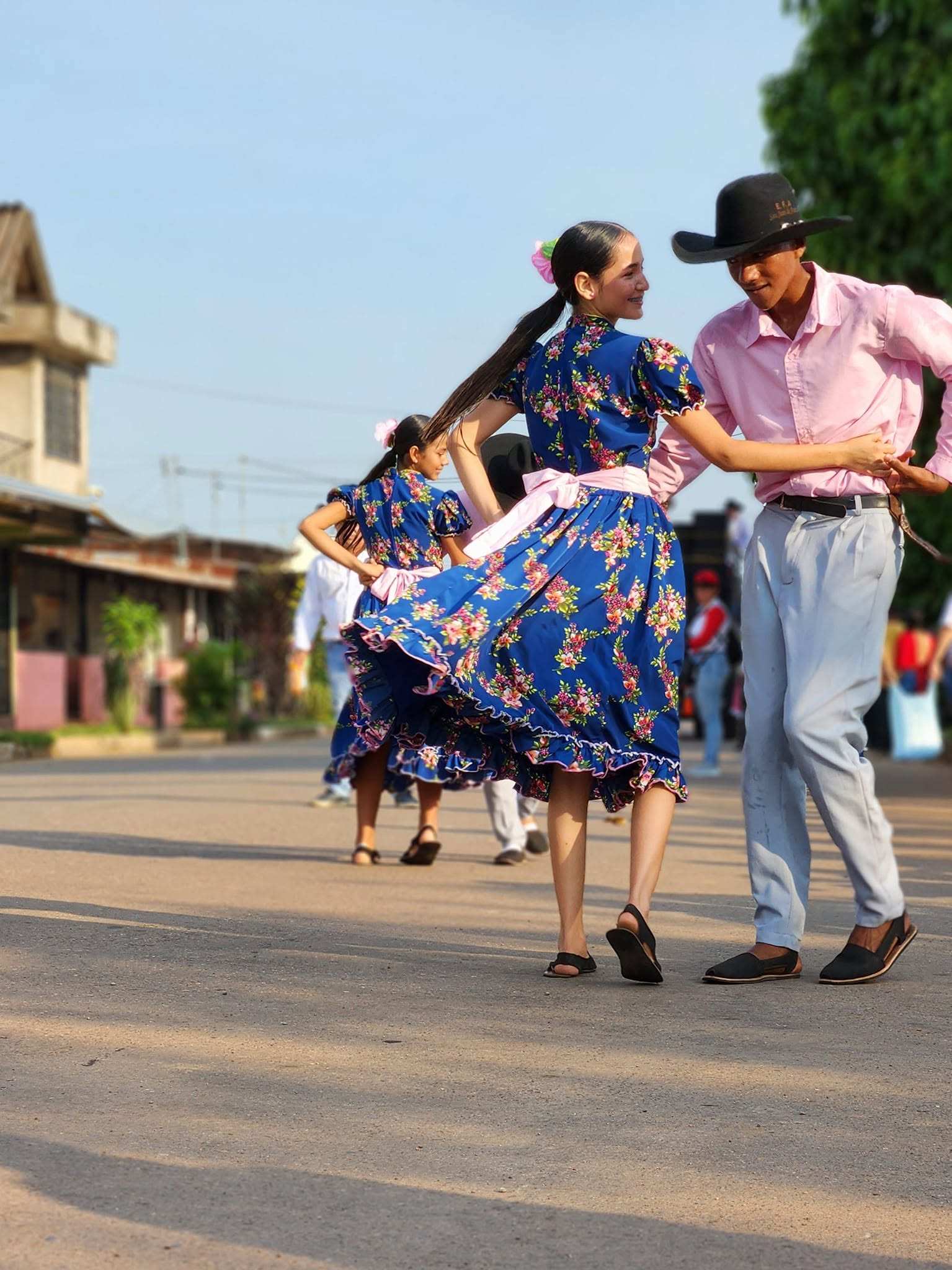 Una pareja baila joropo en la calle: ella con falda azul de flores, él de camisa rosada y sombrero negro.