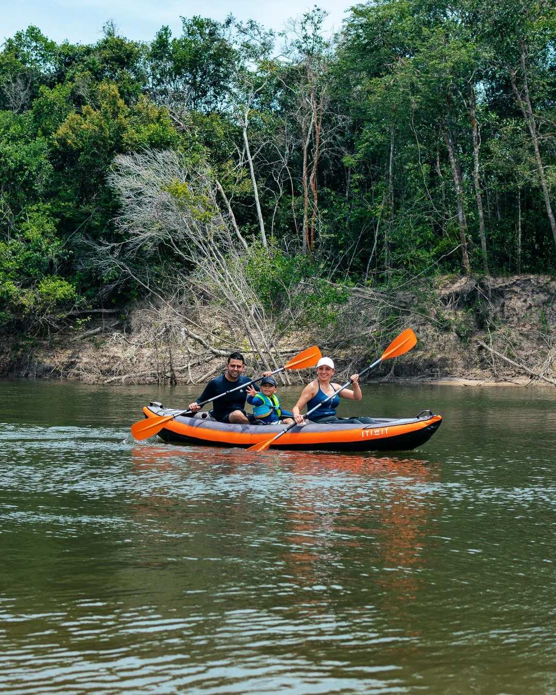 Dos personas reman en un kayak naranja por un río entre el monte.