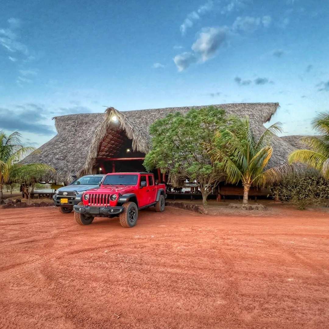 El kiosco grande de techo de palma, con una camioneta roja enfrente sobre la tierra roja.