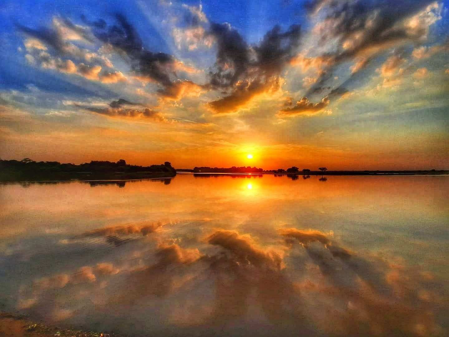 Atardecer sobre la laguna de La Primavera: el sol y las nubes se reflejan en el agua quieta.