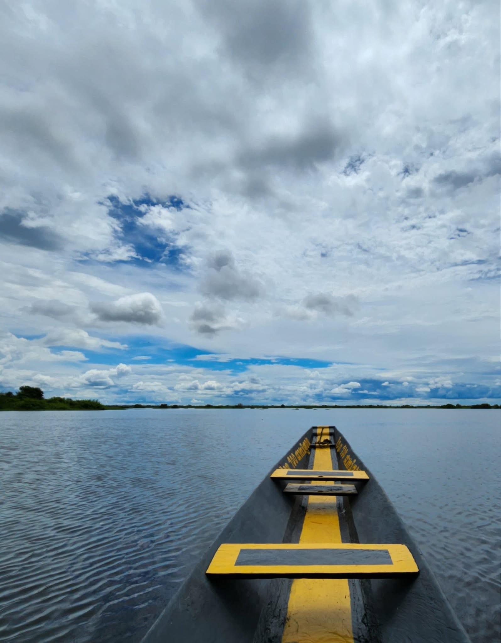 Proa de una canoa pintada de amarillo navegando por la laguna bajo un cielo de nubes.
