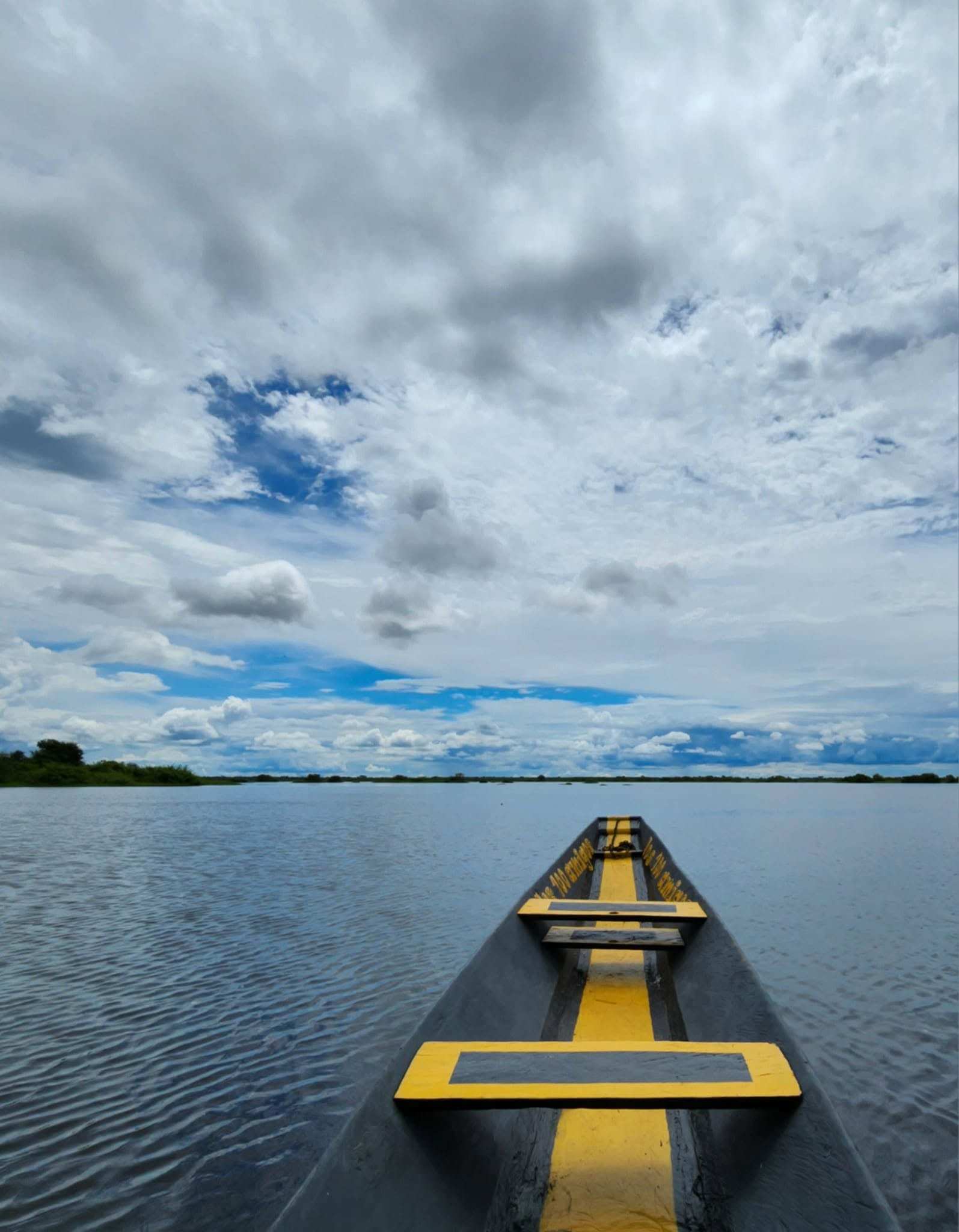 Proa de una canoa pintada de amarillo navegando por la laguna bajo un cielo de nubes.