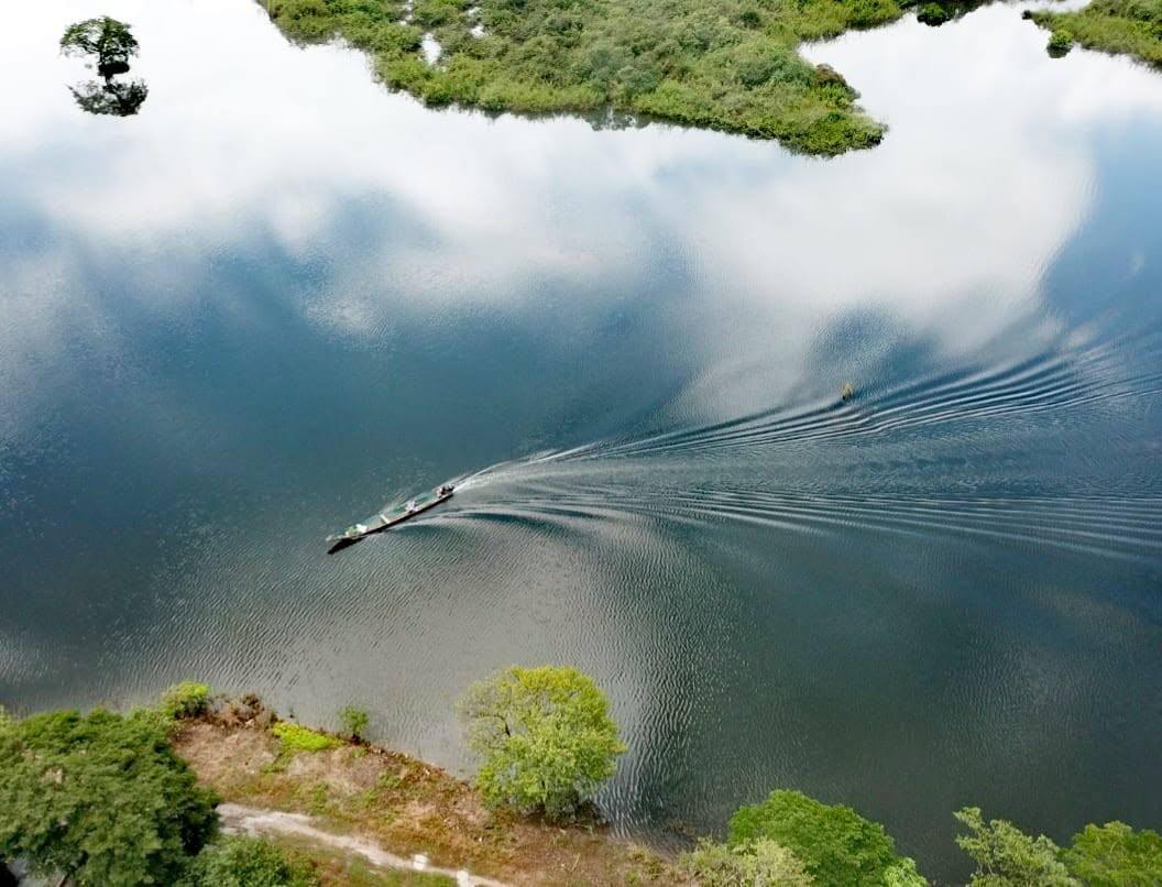 Una lancha deja estela sobre el agua que refleja las nubes.