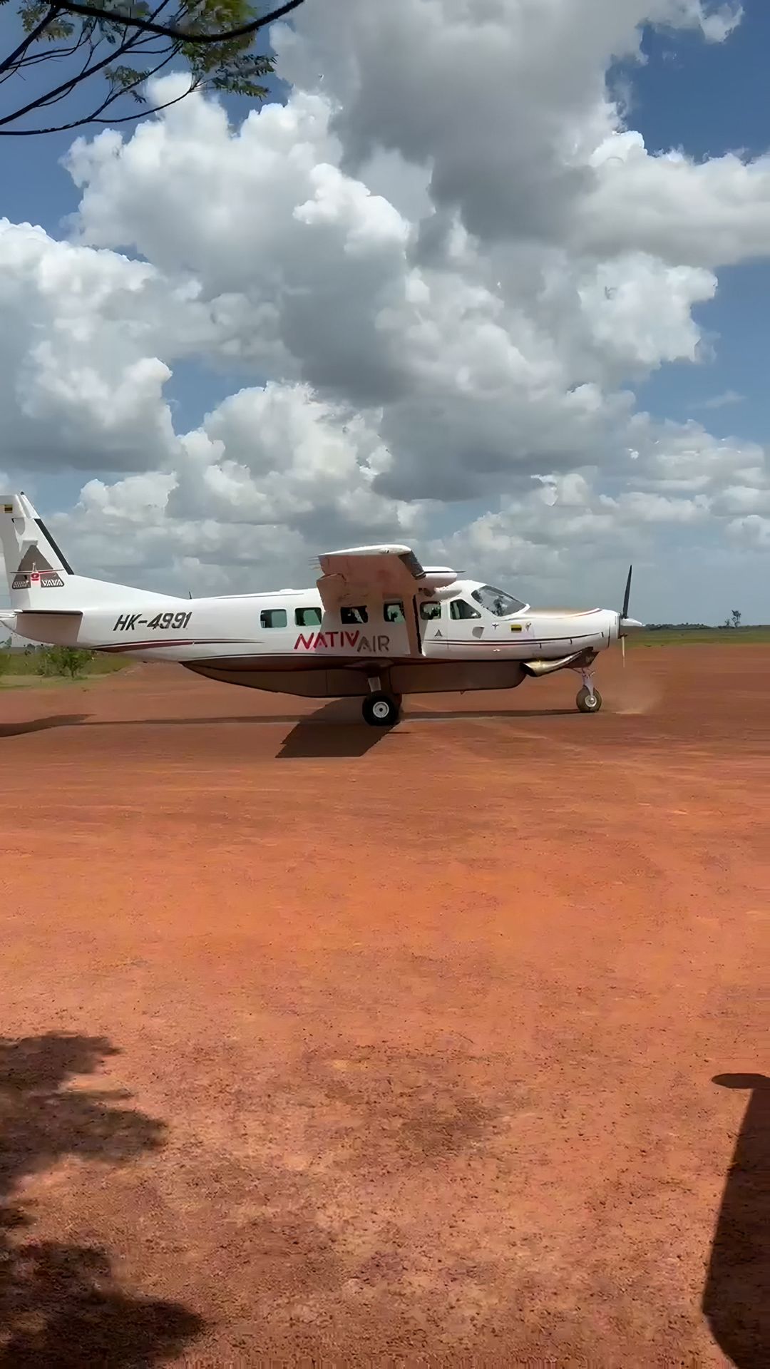 La avioneta de Native sobre la pista de tierra roja, bajo nubes grandes.