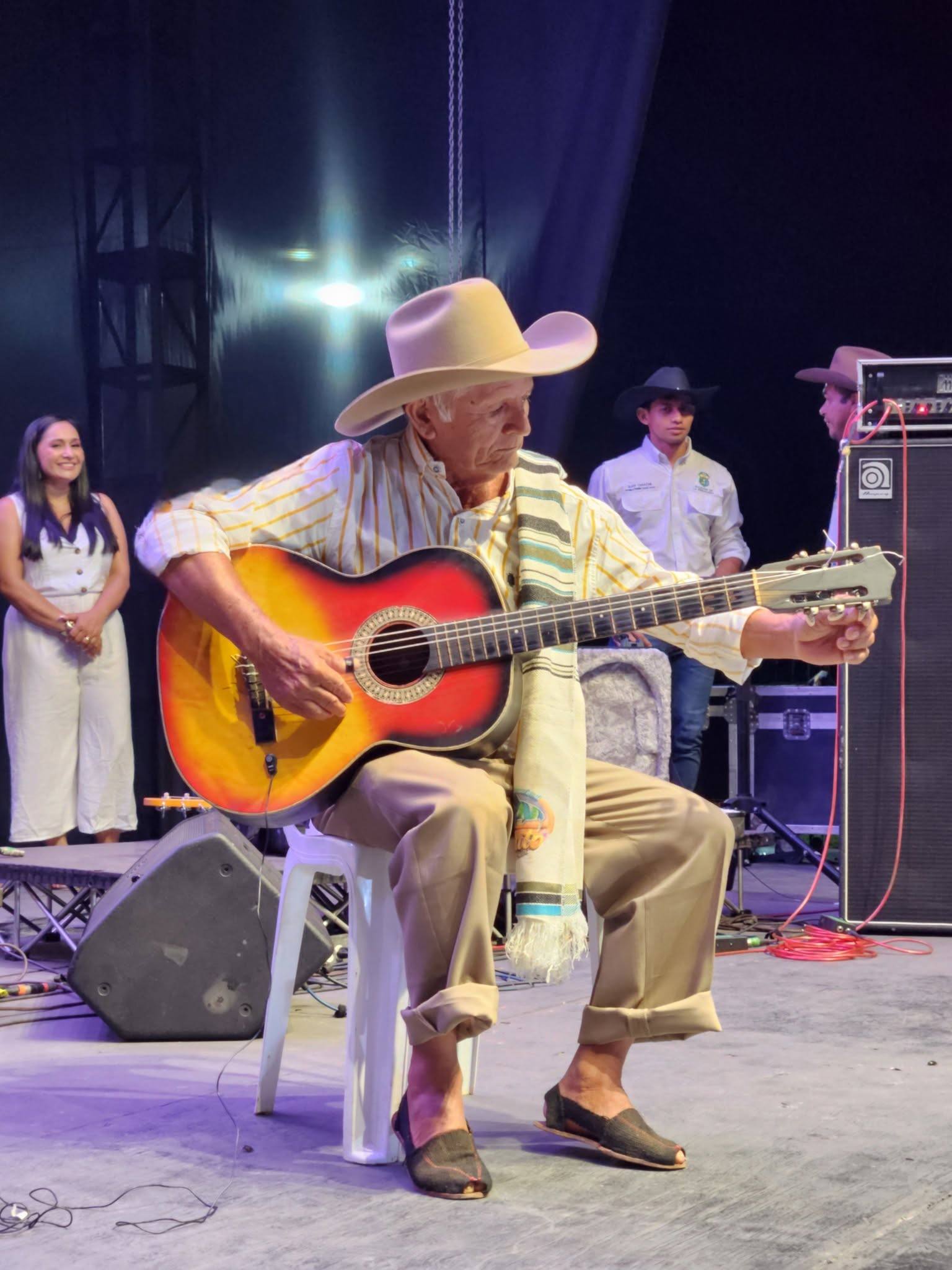 El maestro Pajarillo, con sombrero y guitarra, sentado en la tarima del festival.