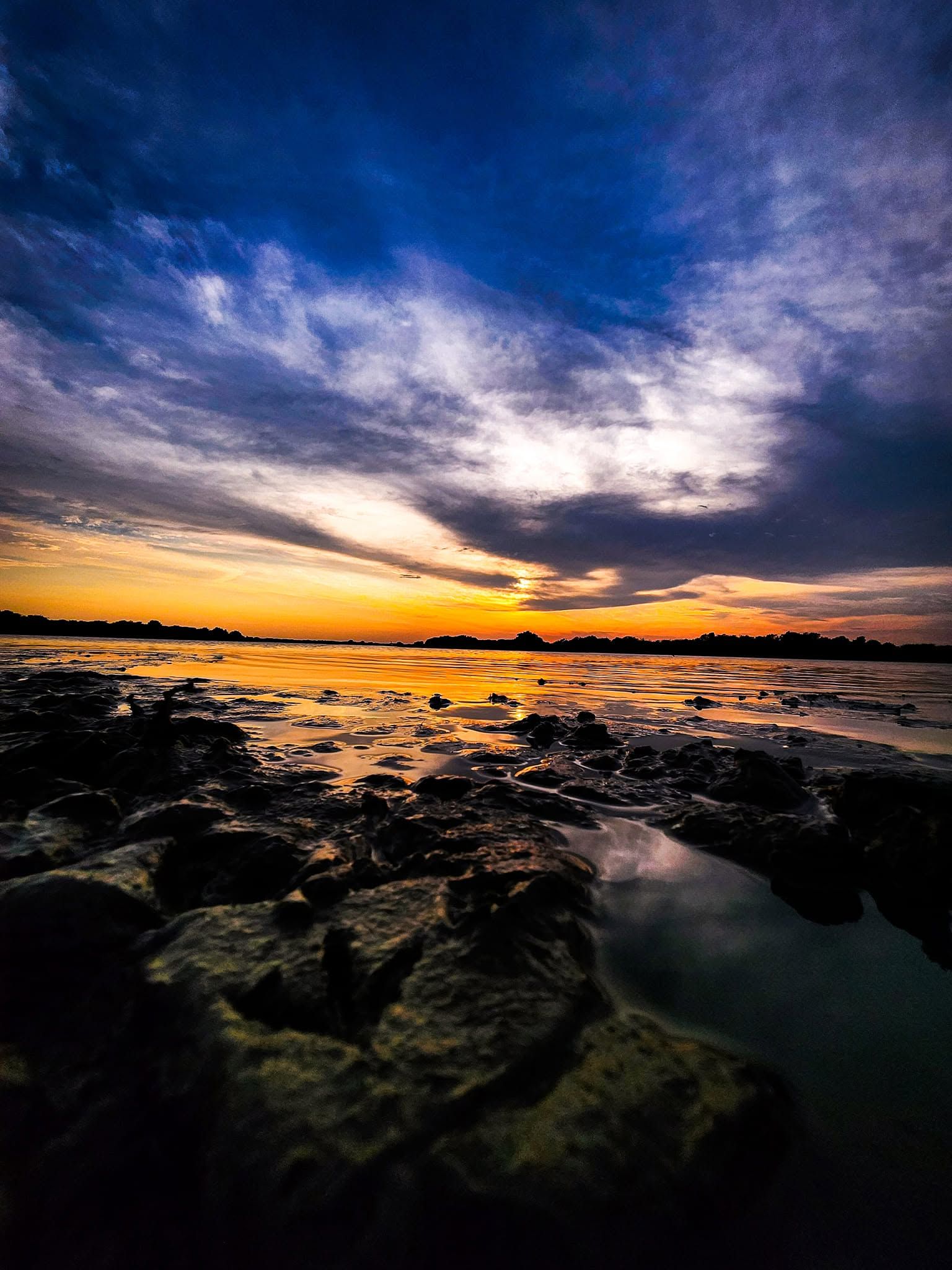 La orilla de lodo seco al atardecer, con el agua baja reflejando el cielo.