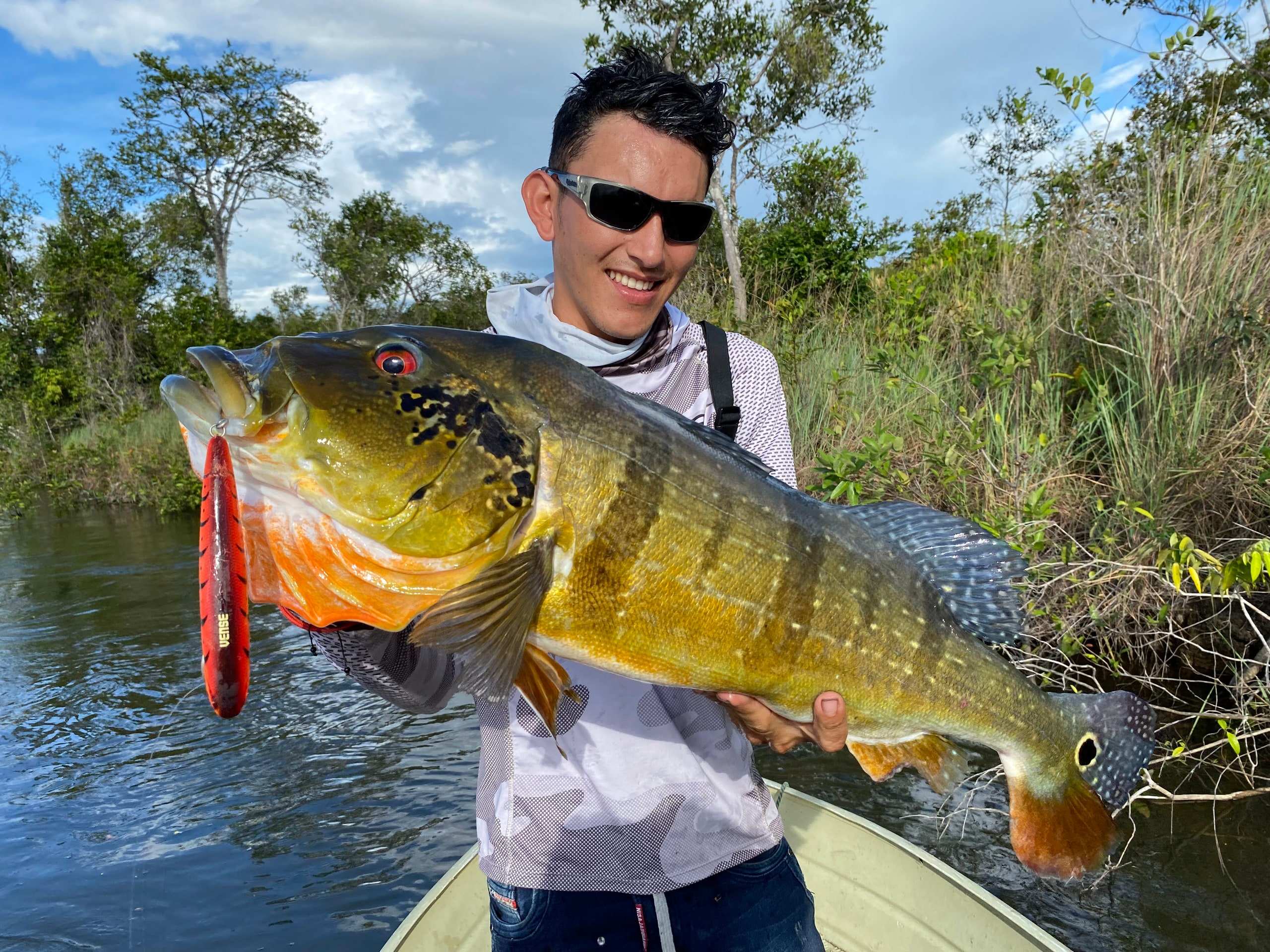 Pescador sonriente con un pavón en una lancha bajo el sol.