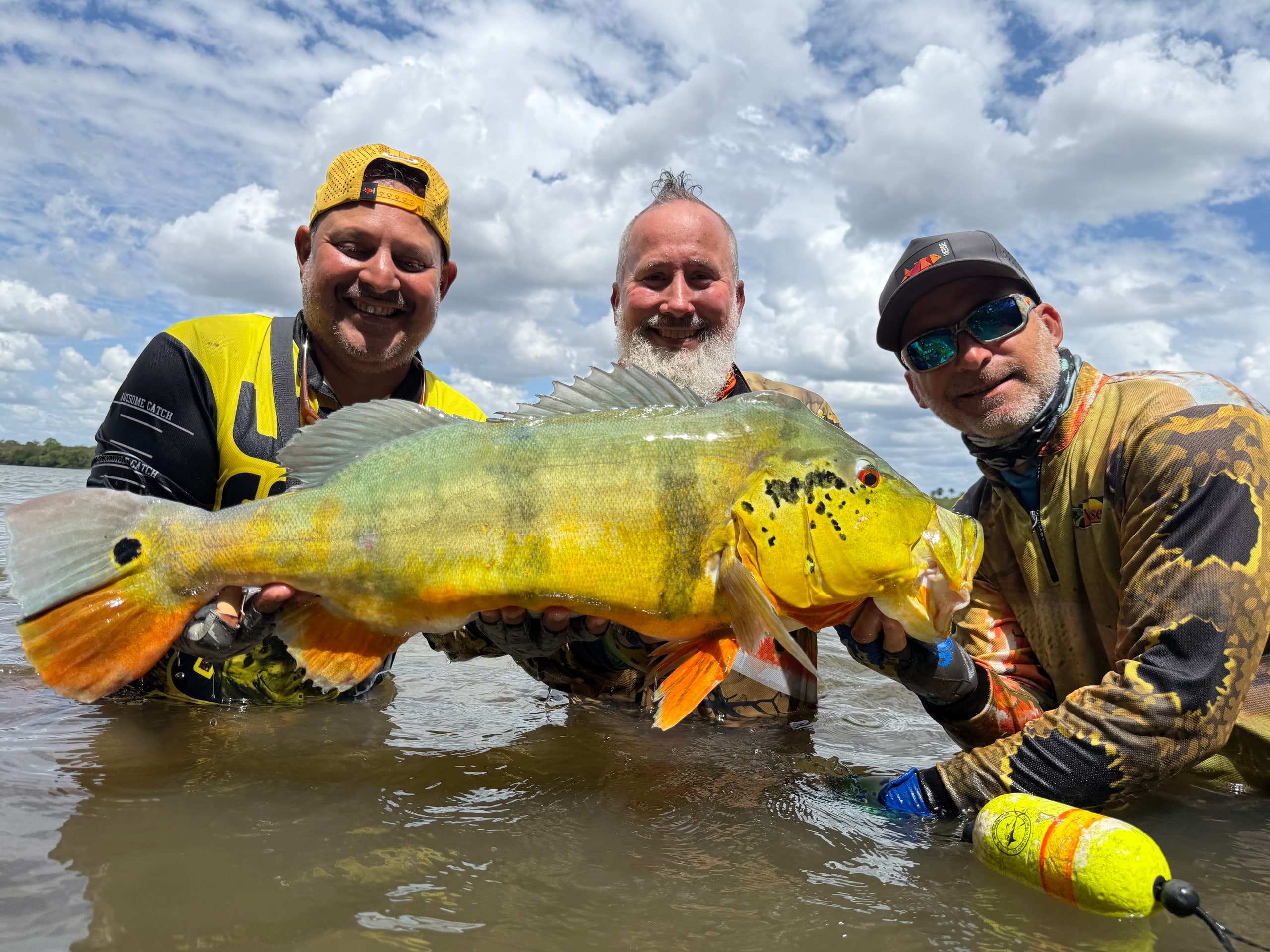 Tres pescadores sostienen juntos un pavón dentro del río.