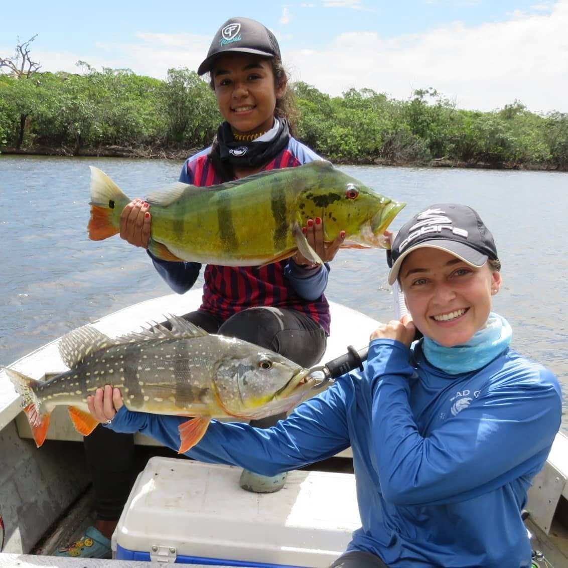 Dos pescadoras en una lancha muestran cada una un pavón.