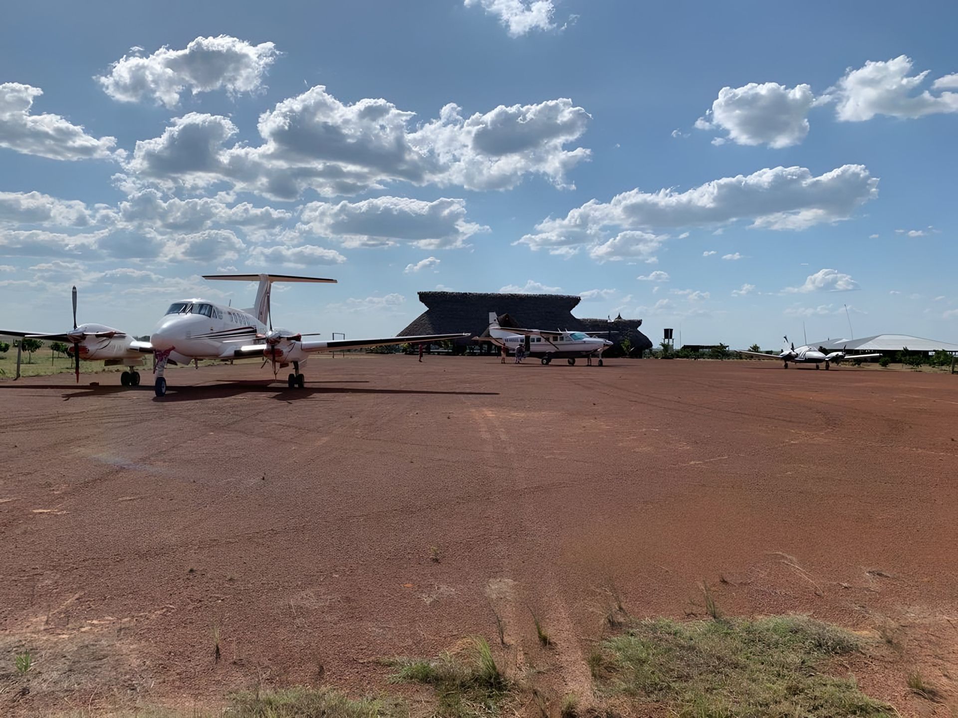 La pista de tierra roja de Native, con sus avionetas y el kiosco de palma bajo un cielo de nubes.