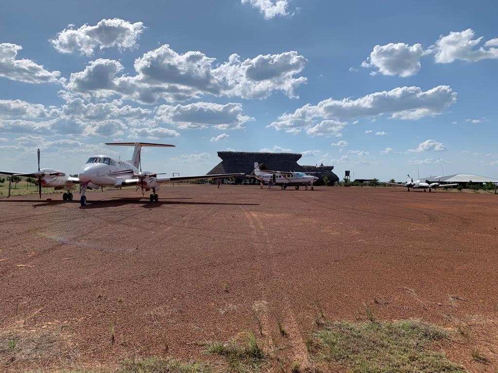 Avionetas en la pista de tierra roja de Native, con el kiosco de palma al fondo.