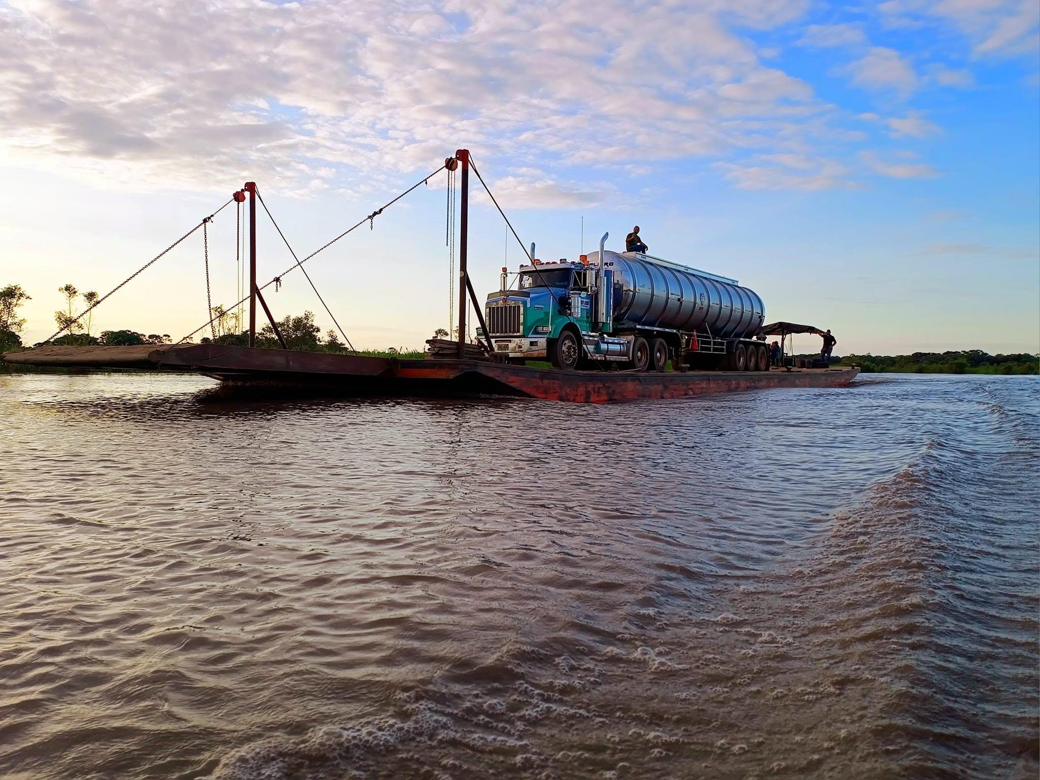 Un camión cisterna cruza el río Meta sobre un planchón, al atardecer.