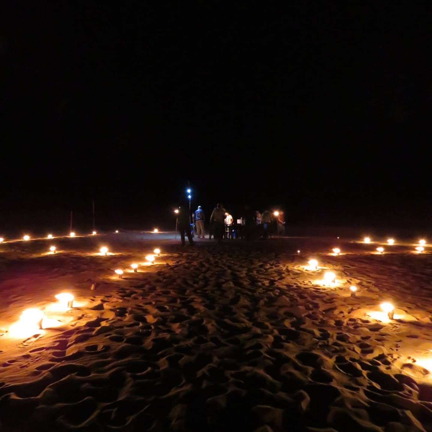 Luces de fogata encendidas en la arena de la playa durante la noche.