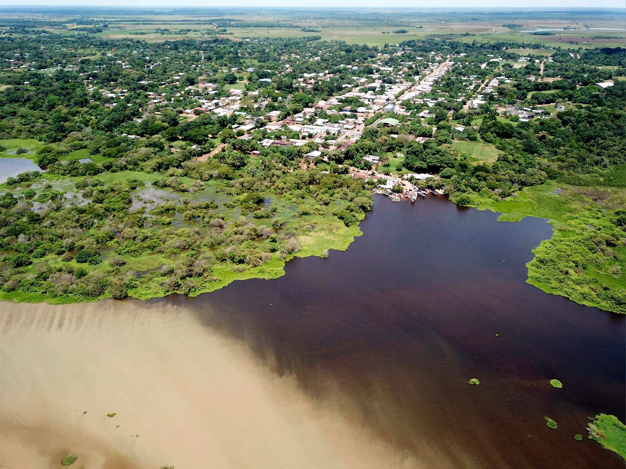 Vista aérea de La Primavera: el pueblo entre árboles, la laguna oscura y el agua café del río Meta que se encuentran frente al puerto.