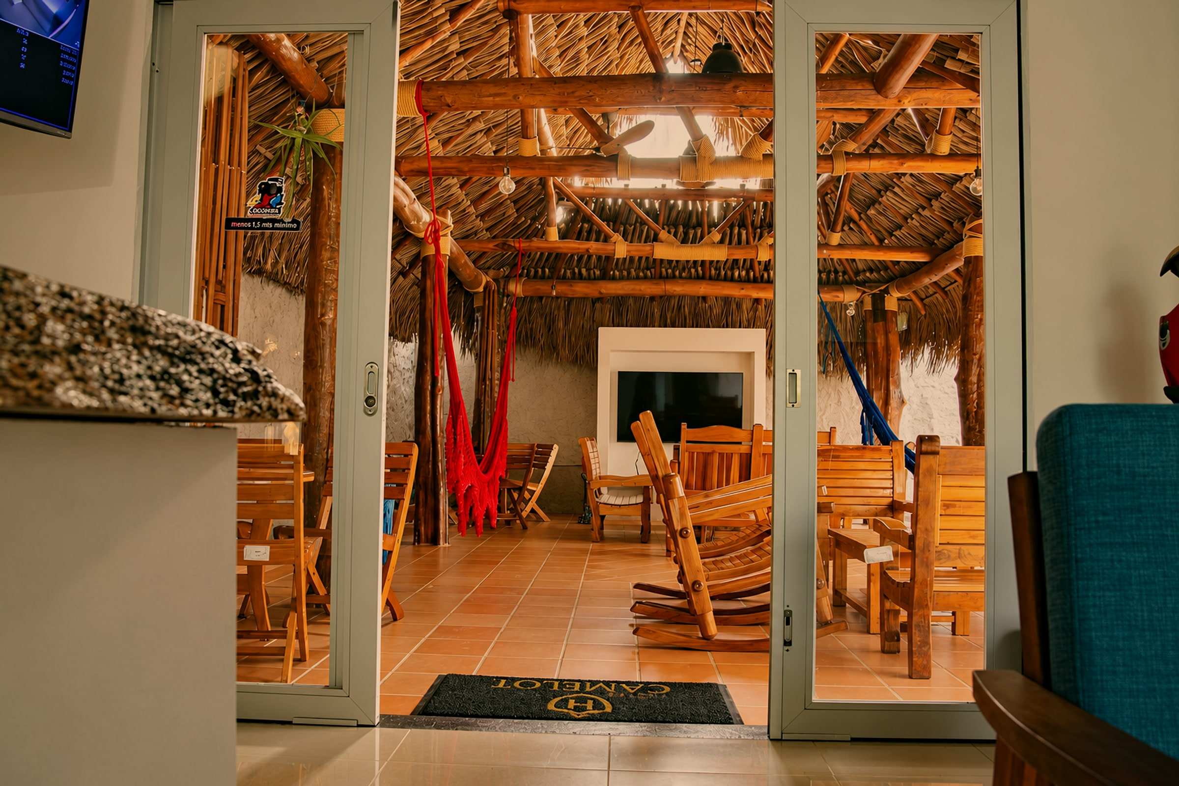 Puertas de vidrio abiertas desde la recepción hacia el kiosko, con hamacas y mesas de madera.