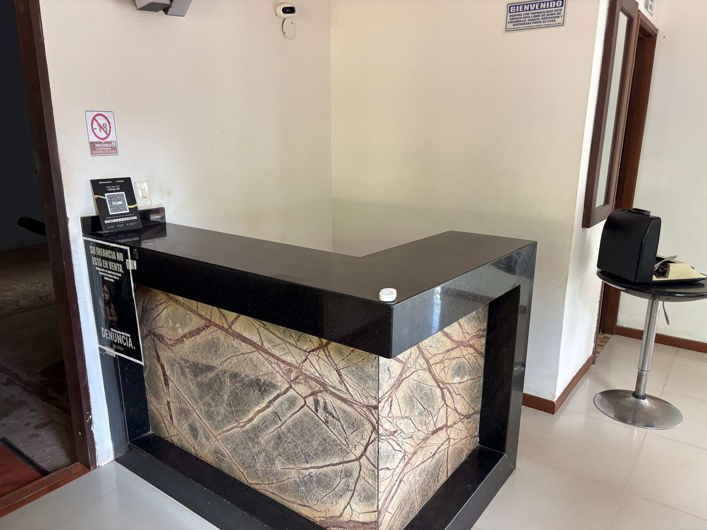 Mostrador de recepción de mármol verde con borde negro y una silla alta al lado.