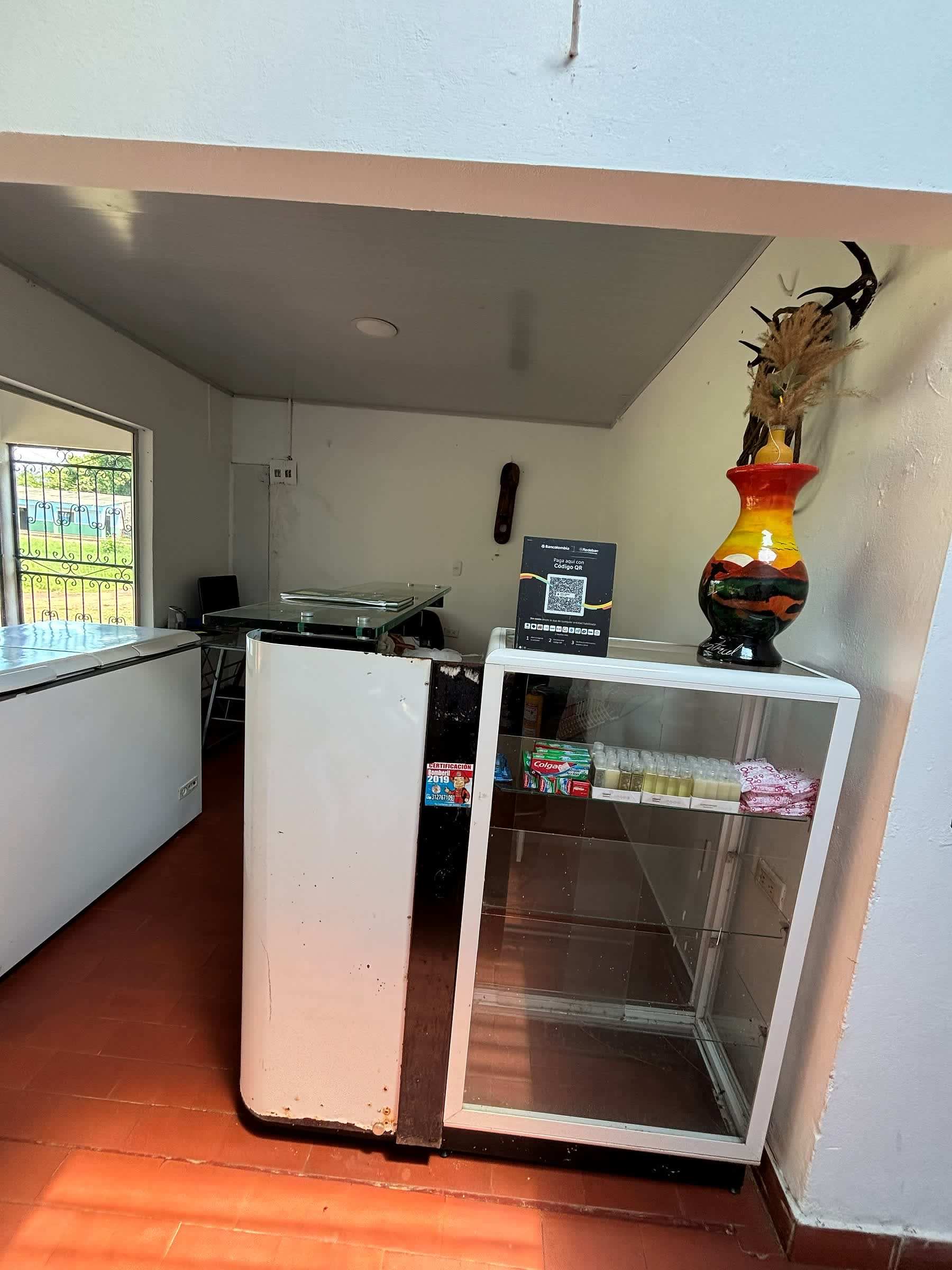 Recepción con mostrador blanco, una vitrina de vidrio y un jarrón de colores.