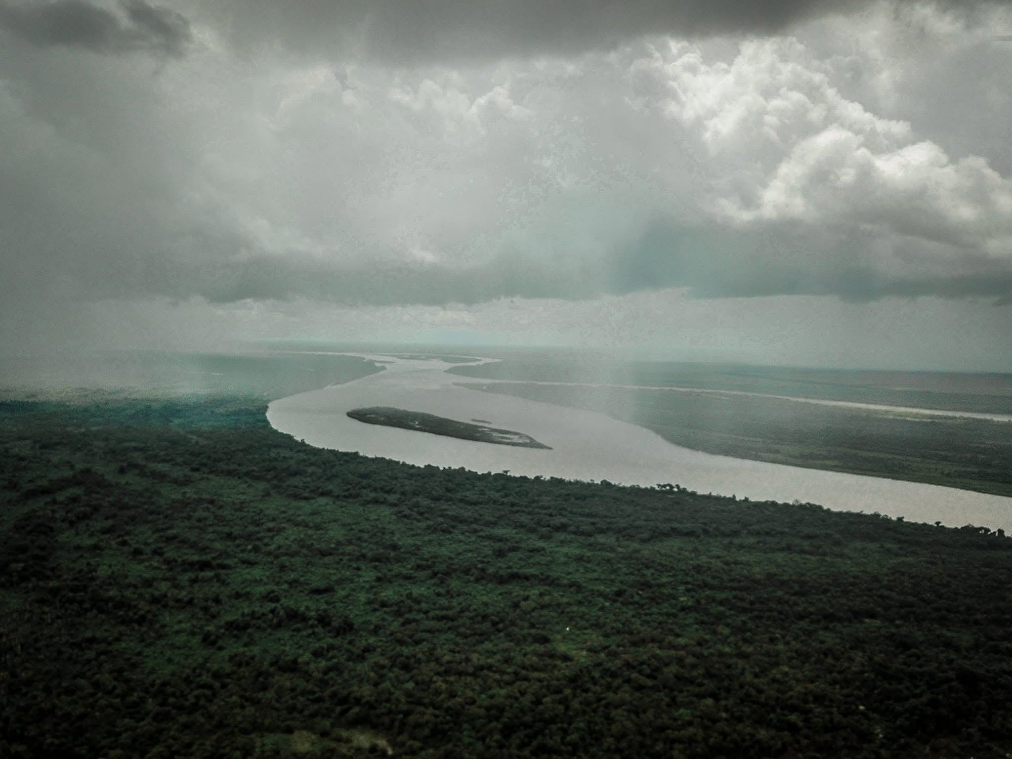 Vista alta del río Meta bajo la lluvia, con una isla en medio y el monte oscuro en la orilla.