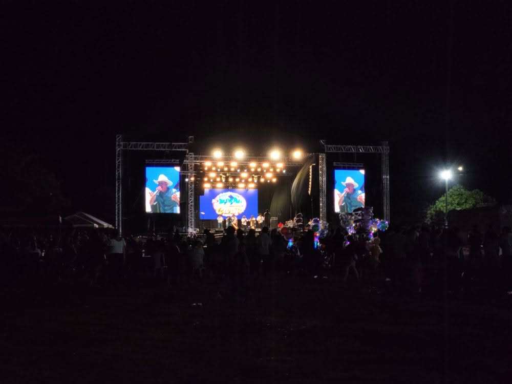 La tarima principal de noche, encendida, con sus pantallas y el público delante.