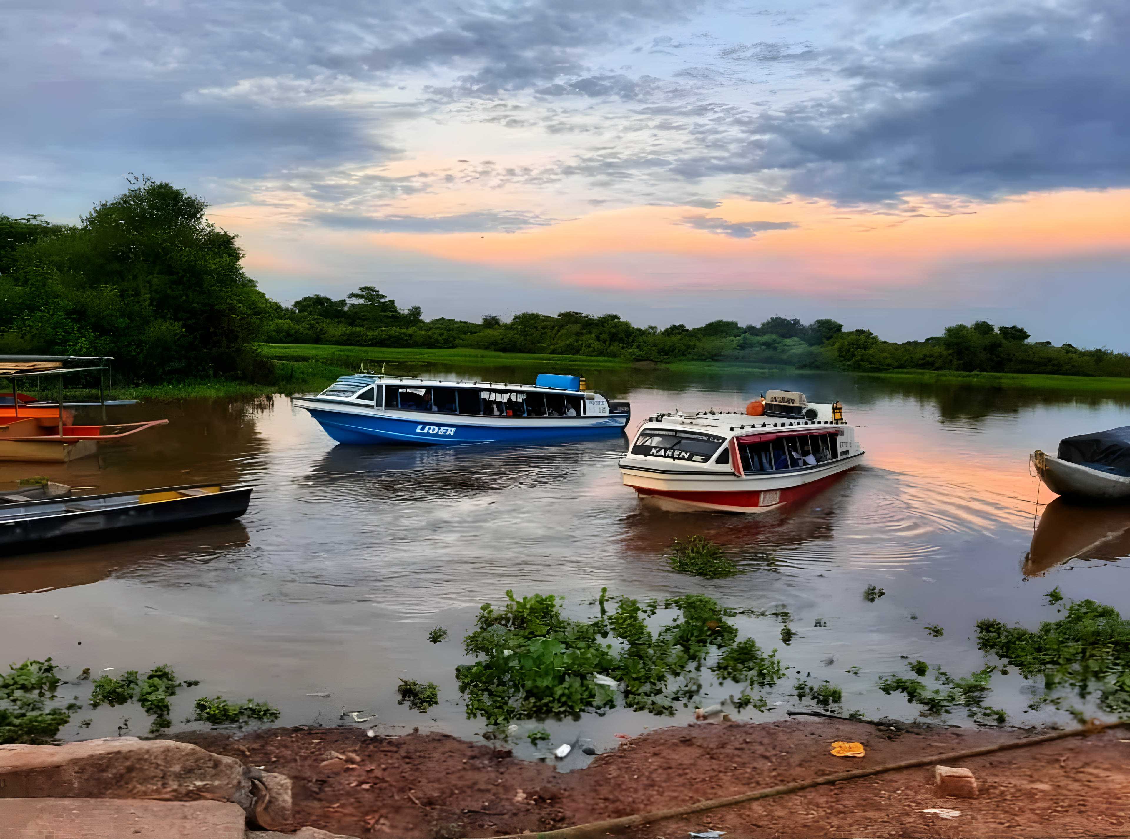 Dos yates de pasajeros, uno azul y uno blanco con rojo, en el agua frente a la orilla de La Primavera al atardecer.